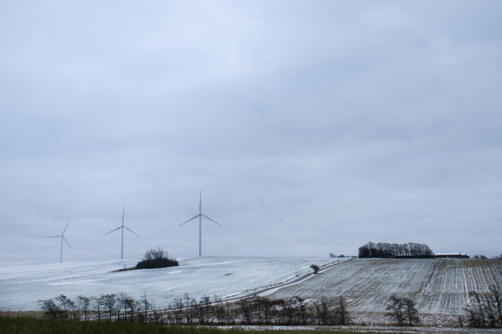 A serene snowy landscape in Randers, Denmark, featuring wind turbines under a cloudy sky.